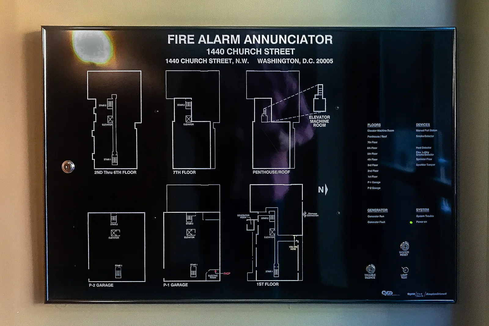 Wall-mounted fire alarm annunciator showing floor plans, device types and trouble silence, reset and lamp test switches