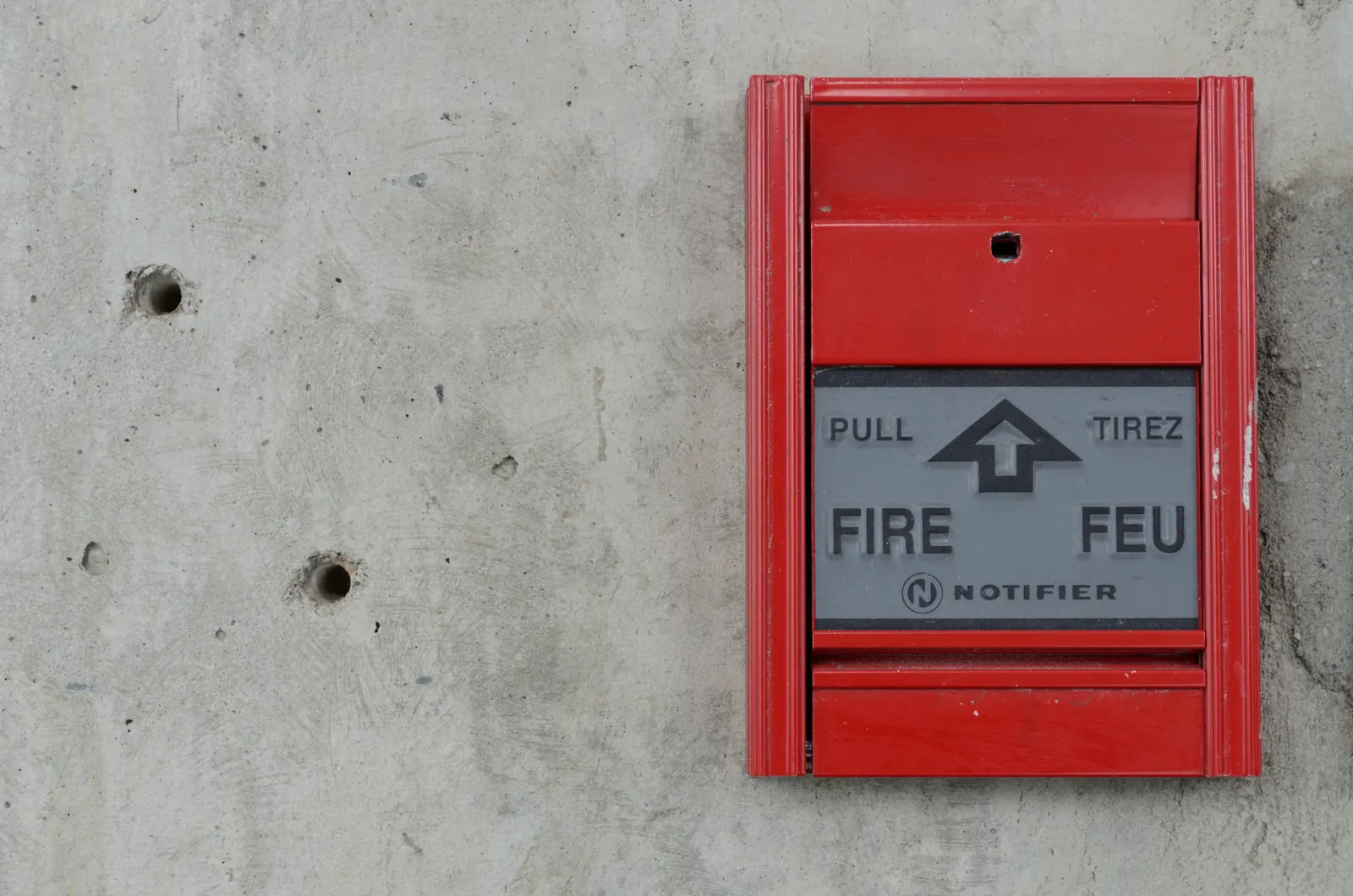 Red Notifier manual pull station on a bare concrete wall, marked PULL and FIRE