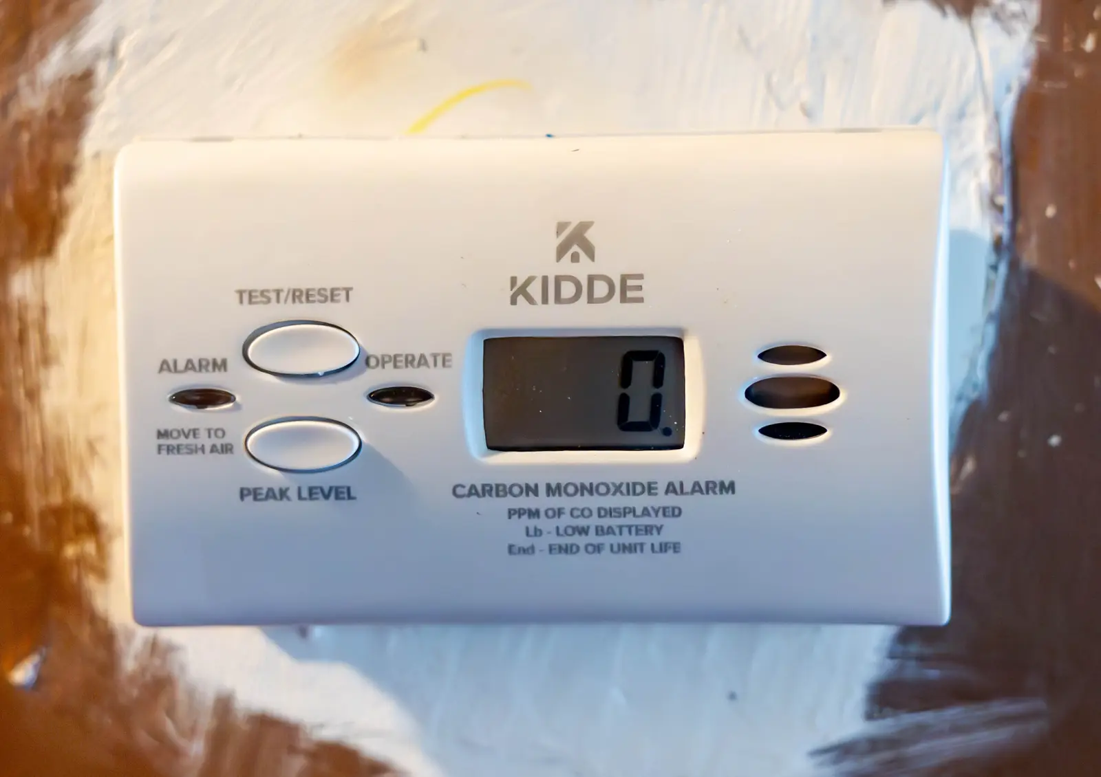 A Kidde carbon monoxide alarm on a wall, its display reading 0, with the labels Lb for low battery and End for end of unit life printed under the screen